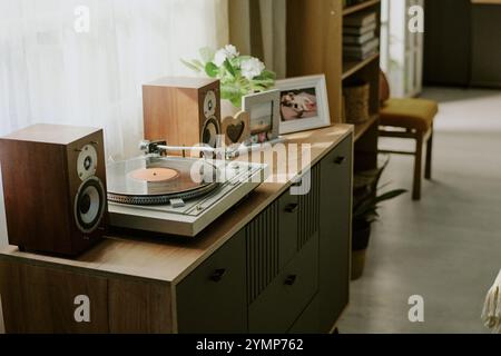 Plateau tournant placé sur une armoire en bois à côté de cadres photo et de plantes en pot avec la lumière du soleil qui coule à travers une fenêtre voisine, créant une ambiance sereine et nostalgique Banque D'Images