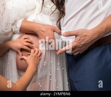 Les mains de l'homme et de la femme forment le cœur sur le ventre des femmes enceintes, les petites mains des enfants forment le cœur. Joie dans l'anticipation du nouveau-né. Famille en anticipation Banque D'Images