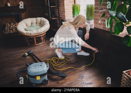 Photo de la brillante femme mignonne habillée chemise blanche allumant l'aspirateur faisant le nettoyage de week-end à l'intérieur de la maison chambre d'appartement Banque D'Images