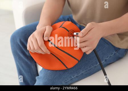 Homme gonflant ballon de basket-ball avec compresseur d'air à l'intérieur, gros plan Banque D'Images