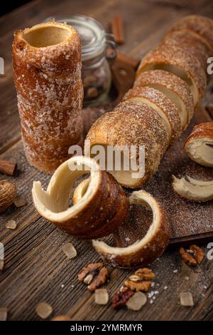 Rouleaux de gâteau de cheminée fraîchement cuits au four avec du sucre et des noix ou des noix de coco sur une table en bois rustique Banque D'Images