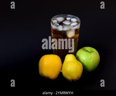 Un mélange de jus de pomme et de poire avec de la glace dans un grand verre sur fond noir, avec des fruits mûrs à proximité. Gros plan. Banque D'Images