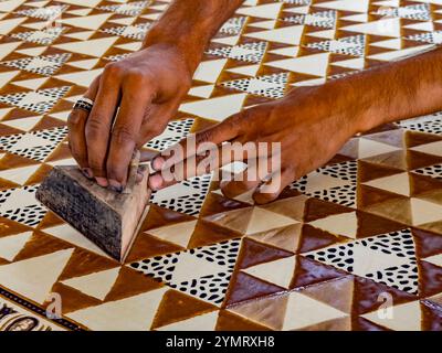 Artisan utilisant la technique traditionnelle d'impression de blocs en bois, appliquant la teinture brune sur le tissu, créant un motif géométrique complexe Banque D'Images