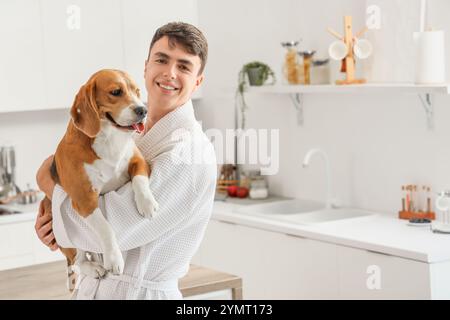 Jeune homme en peignoir tenant le chien Beagle mignon dans la cuisine Banque D'Images
