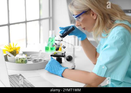 Scientifique féminine avec microscope et ordinateur portable testant les germes de tournesol en laboratoire Banque D'Images