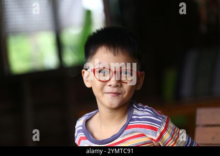 Un jeune garçon joyeux avec des lunettes pose dans un cadre intérieur décontracté, mettant en valeur son esprit ludique et sa personnalité joyeuse. Couleurs vives et lumière chaude Banque D'Images