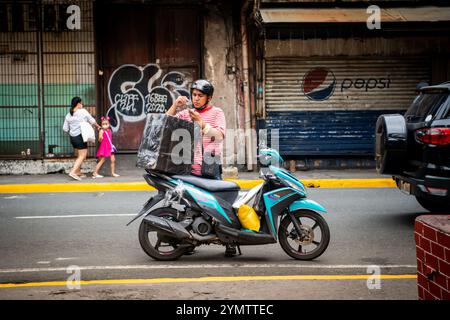 Un philippin emballe une grosse valise sur son cyclomoteur dans la région d'Ermita à Manille, aux Philippines. Banque D'Images