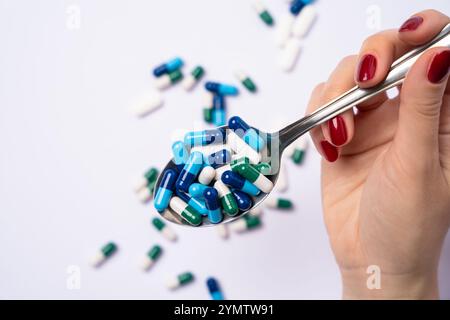 Main femelle tenant cuillère en métal avec beaucoup de pilules pharmaceutiques assorties et capsules colorées. Capsules et pilules de médicaments en arrière-plan. Vue de dessus Banque D'Images