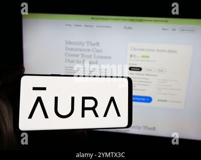 Dans cette illustration photo, une personne tient un smartphone avec le logo de la société américaine de logiciels de cybersécurité aura Sub LLC en face du site Web. Banque D'Images