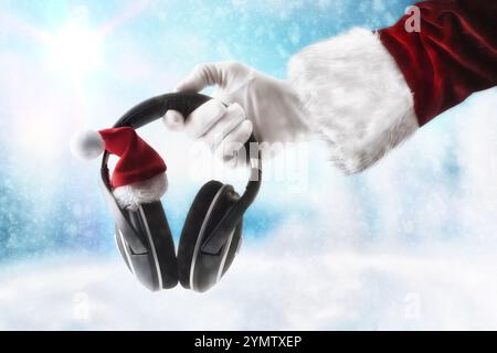 Mains du Père Noël tenant des écouteurs pour écouter la musique de Noël décorée avec chapeau de Père Noël et fond de paysage enneigé. Banque D'Images