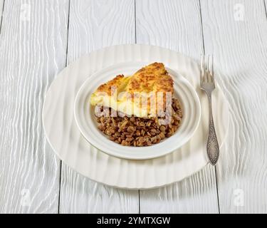 tarte végétalienne aux bergers de lentilles cuites garnie de purée de pommes de terre sur assiette blanche avec fourchette sur table en bois, vue horizontale d'en haut, gros plan Banque D'Images