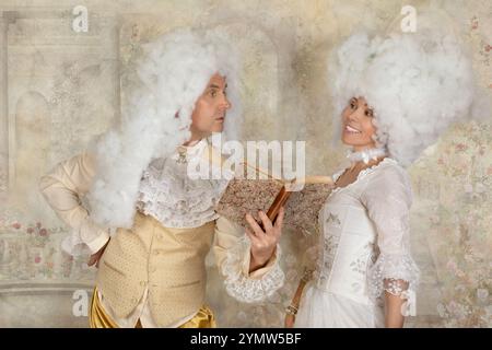 Couple mignon dans des vêtements de style baroque lisant un livre à l'intérieur Banque D'Images