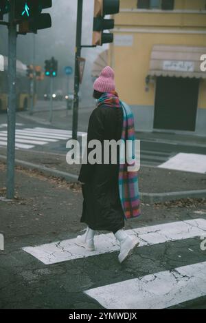 Une femme qui porte un chapeau rose et une écharpe rose traverse la rue Banque D'Images