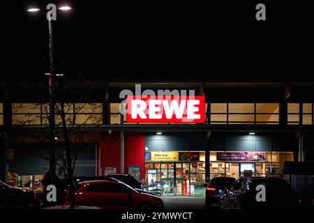 Erding, Bavière, Allemagne - 22 novembre 2024 : supermarché REWE la nuit. L'entrée d'un supermarché Rewe, illuminée par le logo rouge frappant et entourée de voitures garées, symbolise l'expérience shopping du soir *** Rewe-Supermarkt BEI Nacht. Der Eingang eines Rewe-Markts, beleuchtet durch das markante rote logo und umgeben von parkenden Autos, symbolisiert das abendliche Einkaufserlebnis Banque D'Images