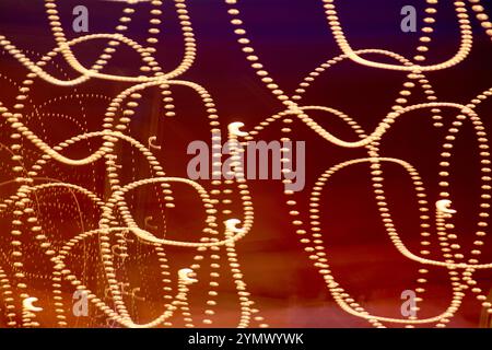 Cette image capture des traînées de lumière abstraites formant des motifs complexes et en boucle sur un fond sombre avec un dégradé du rouge au bleu, créant ainsi Banque D'Images