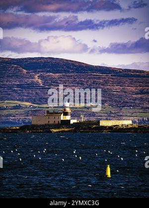 Un phare blanc avec un toit rouge est situé sur une petite île, entourée d'eau bleue. L'île est recouverte de roches sombres. Banque D'Images