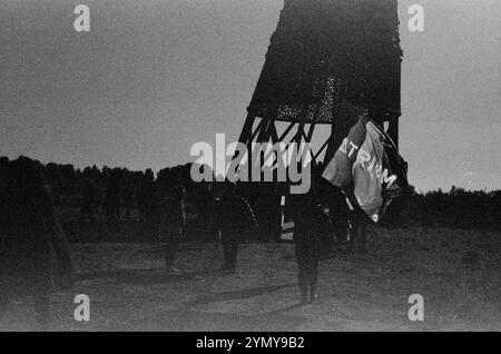 Dans la photographie monochrome, un homme se tient devant une tour, tenant un drapeau, sous un ciel dégagé, film 35mm Banque D'Images