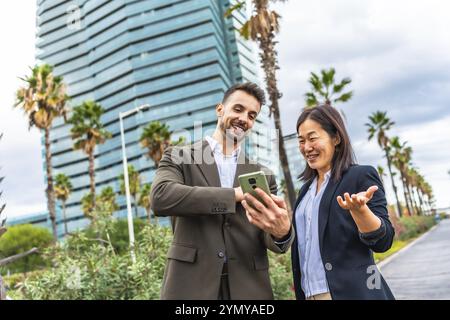 Heureux gens d'affaires multiraciaux regardant le téléphone portable et souriant debout dans la ville Banque D'Images
