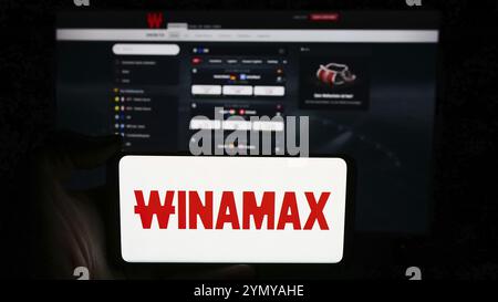 Stuttgart, Allemagne, 06-06-2024 : personne tenant un téléphone portable avec le logo de la société française de Paris sportifs Winamax sa en face de la page web de l'entreprise. Concentrez-vous sur Banque D'Images