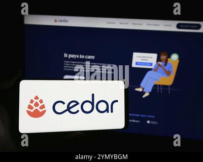 Stuttgart, Allemagne, 03-06-2024 : personne tenant un smartphone avec le logo de la société américaine de logiciels de soins de santé Cedar Cares Inc. en face du site Web. Concentrez-vous sur p. Banque D'Images