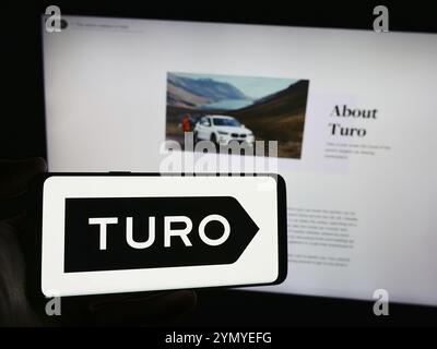 Stuttgart, Allemagne, 03-18-03 2024 : personne tenant un smartphone avec le logo de la société américaine d'autopartage peer-to-peer Turo Inc devant le site Web. Concentrez-vous sur le phon Banque D'Images