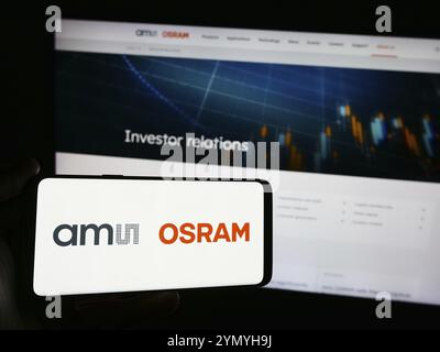 Stuttgart, Allemagne, 05-31-2024, personne tenant un smartphone avec le logo de la société autrichienne d'électronique AMS OSRAM AG devant le site. Concentrez-vous sur le téléphone d Banque D'Images