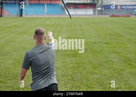 Athlète masculin s'engageant dans un lancer de javelot sur un grand terrain ouvert avec les environs du stade visible. Figure athlétique participant activement à un événement sportif de plein air Banque D'Images
