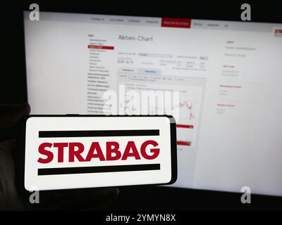 Stuttgart, Allemagne, 04-15-2024 : personne tenant un téléphone portable avec le logo de l'entreprise de construction autrichienne Strabag se en face de la page Web de l'entreprise. Mise au point Banque D'Images