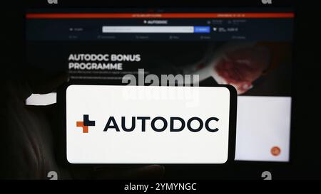 Stuttgart, Allemagne, 05-24-2024 : personne tenant un téléphone portable avec le logo de la société allemande de commerce électronique de pièces automobiles Autodoc se en face de la page Web de l'entreprise. FOC Banque D'Images