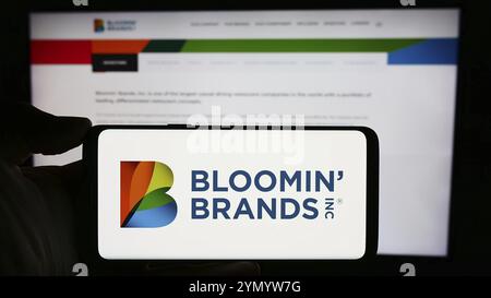Stuttgart, Allemagne, 03-13-2024 : personne tenant un téléphone portable avec le logo de la société holding de restaurant américaine Bloomin' Brands Inc en face de la page Web de l'entreprise. Banque D'Images