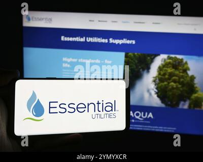 Stuttgart, Allemagne, 07-06-2024 : personne tenant un téléphone portable avec le logo de la société américaine Essential Utilities Inc devant la page web. Banque D'Images
