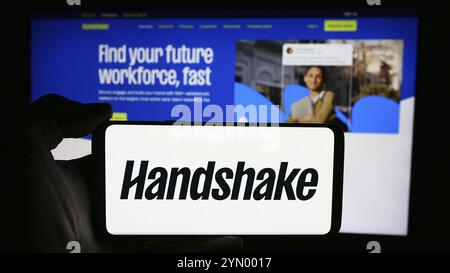 Stuttgart, Allemagne, 06-03-2024 : personne tenant un téléphone portable avec le logo de la société américaine de logiciels de recrutement Stryder Corp. (Handshake) devant le webpa Banque D'Images