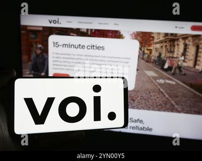 Stuttgart, Allemagne, 05-14-2024 : personne tenant un téléphone portable avec le logo de la société suédoise de scooter électrique VOI Technology AB en face de la page Web de l'entreprise. Banque D'Images