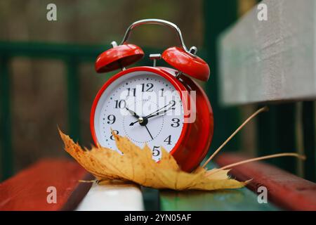 Heure d'automne. Réveil et feuille tombée sur banc en bois à l'extérieur Banque D'Images