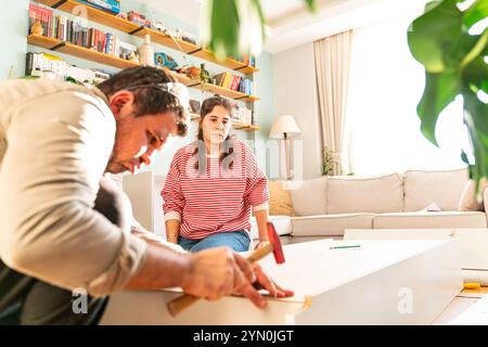 Jeune couple vient de se marier en assemblant un meuble dans leur maison. Avec un tournevis et des outils à la main pour suivre le manuel d'instructions. Banque D'Images