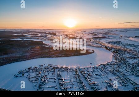 Lever de soleil sur un paysage enneigé révélant une rivière et un village calme pendant l'hiver dans la campagne Banque D'Images