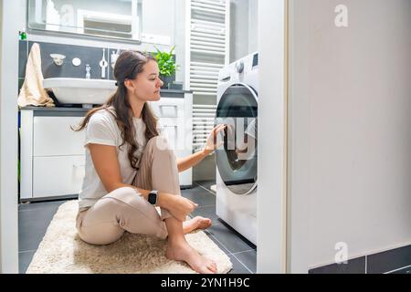 Jeune femme attendant que la machine à laver finisse, regardant la porte de la machine à laver Banque D'Images