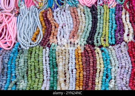 Une variété de colliers et bracelets de perles colorés disposés sur une surface. Certaines perles sont rondes et lisses, tandis que d'autres sont de forme irrégulière. Banque D'Images