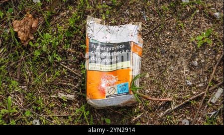 Paquet de cigarettes jeté couché sur le sol au milieu de l'herbe et de la saleté, soulignant la pollution environnementale Banque D'Images