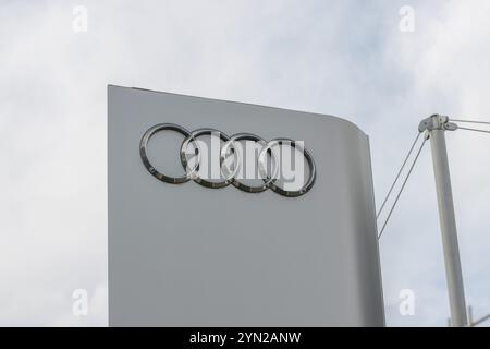 Logo audi chromé monté sur un bâtiment de concession sous un ciel nuageux Banque D'Images