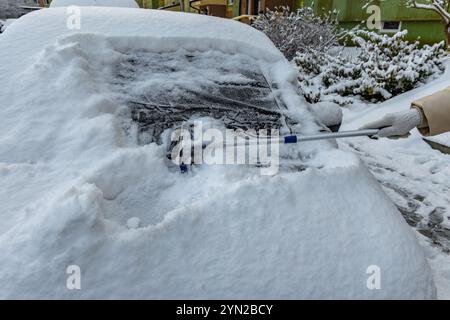 Une femme pelle la neige de la voiture, enlevant la glace de la carrosserie, attaque hivernale, préparant la voiture pour l'itinéraire Banque D'Images