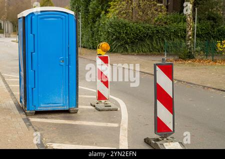 Toilettes portatives bleues dans une rue à côté de poteaux d'avertissement de circulation indiquant des travaux routiers Banque D'Images