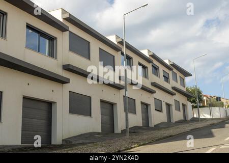 Architecture résidentielle avec une rangée de maisons de ville contemporaines avec garages intégrés, situées sur une rue en pente Banque D'Images