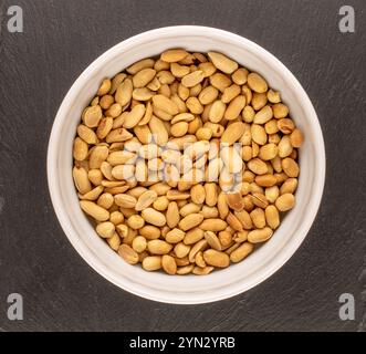 Cacahuètes pelées, grillées dans une plaque de céramique sur une pierre d'ardoise, macro, vue de dessus. Banque D'Images