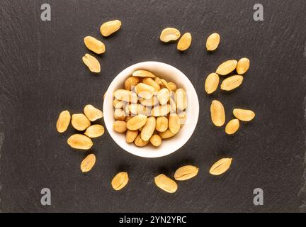 Cacahuètes pelées, grillées dans une plaque de céramique sur une pierre d'ardoise, macro, vue de dessus. Banque D'Images