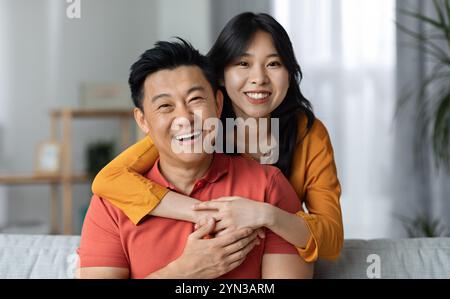 Homme et femme asiatiques heureux se posant ensemble chez eux Banque D'Images