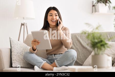 Heureuse fille asiatique uing tablette et racontant des nouvelles à un ami Banque D'Images