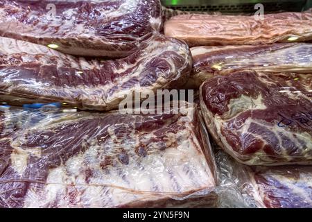 Grands morceaux de viande réfrigérée crue emballés sous vide dans la vitrine de boucherie. Banque D'Images