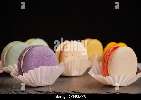 Macarons multicolores magnifiquement conçus sur un fond noir. Une merveilleuse présentation de pâtisseries exquises et de bonbons d'origine française Banque D'Images