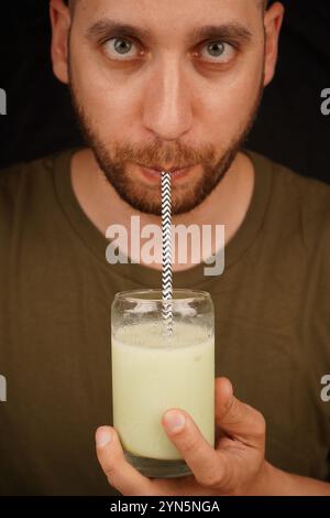 Gros plan d'un homme buvant du matcha latte vert dans un verre à travers une paille, concept de culture du thé. Un homme sirote du thé à travers une paille Banque D'Images